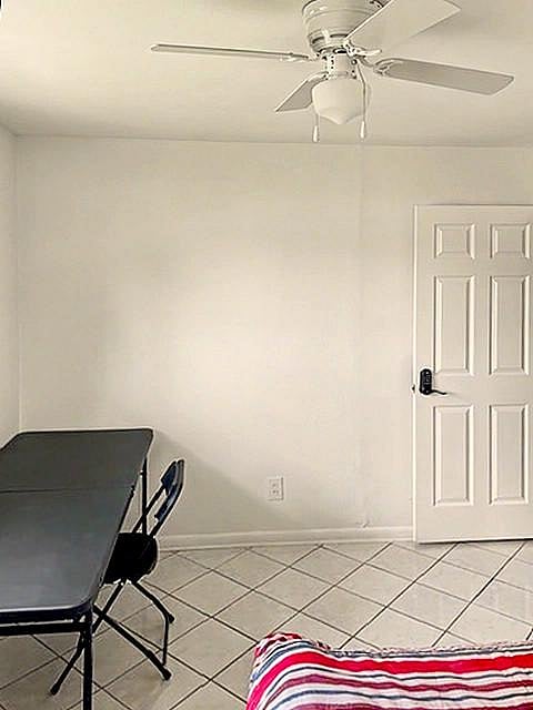 Simple bedroom with tile flooring, ceiling fan, and space for a bed plus a small desk or seating area.
