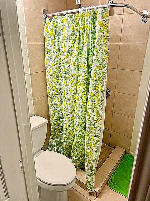 Space-saving bathroom with tiled walk-in shower, curtain rod, and standard toilet layout for easy daily use.