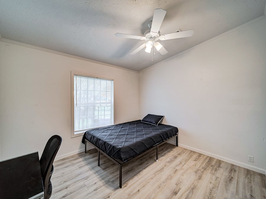 Private bedroom with wood-look flooring, a large window with blinds, and a ceiling fan with light for year-round comfort.