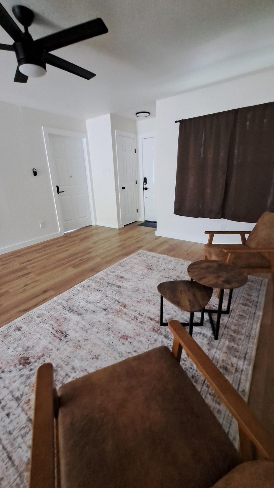 Open living area with wood-style floors, ceiling fan, and space for seating near the entry and window.