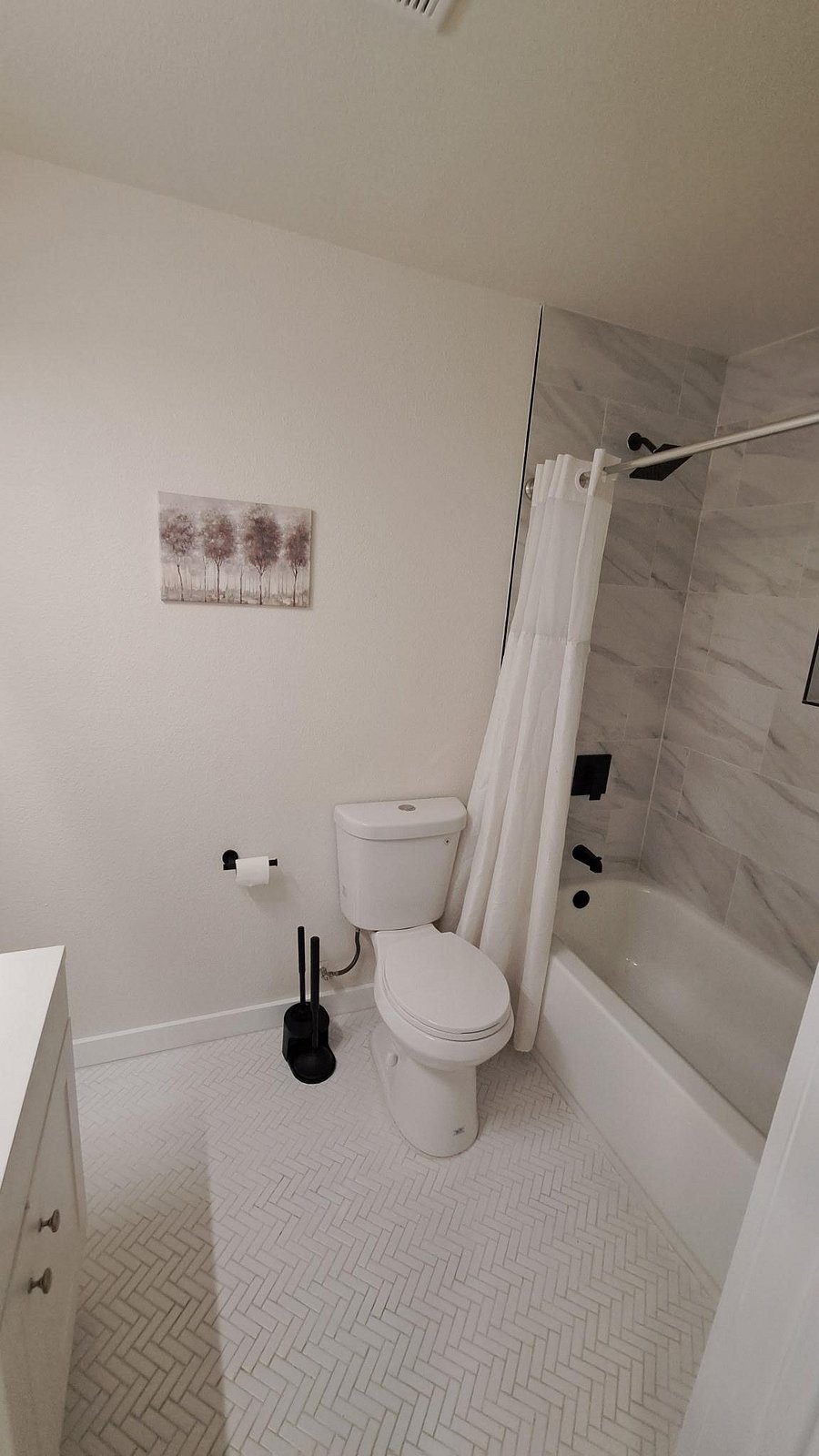 Clean full bath with tub/shower combo, tile surround, and matte-black fixtures, plus herringbone tile flooring.