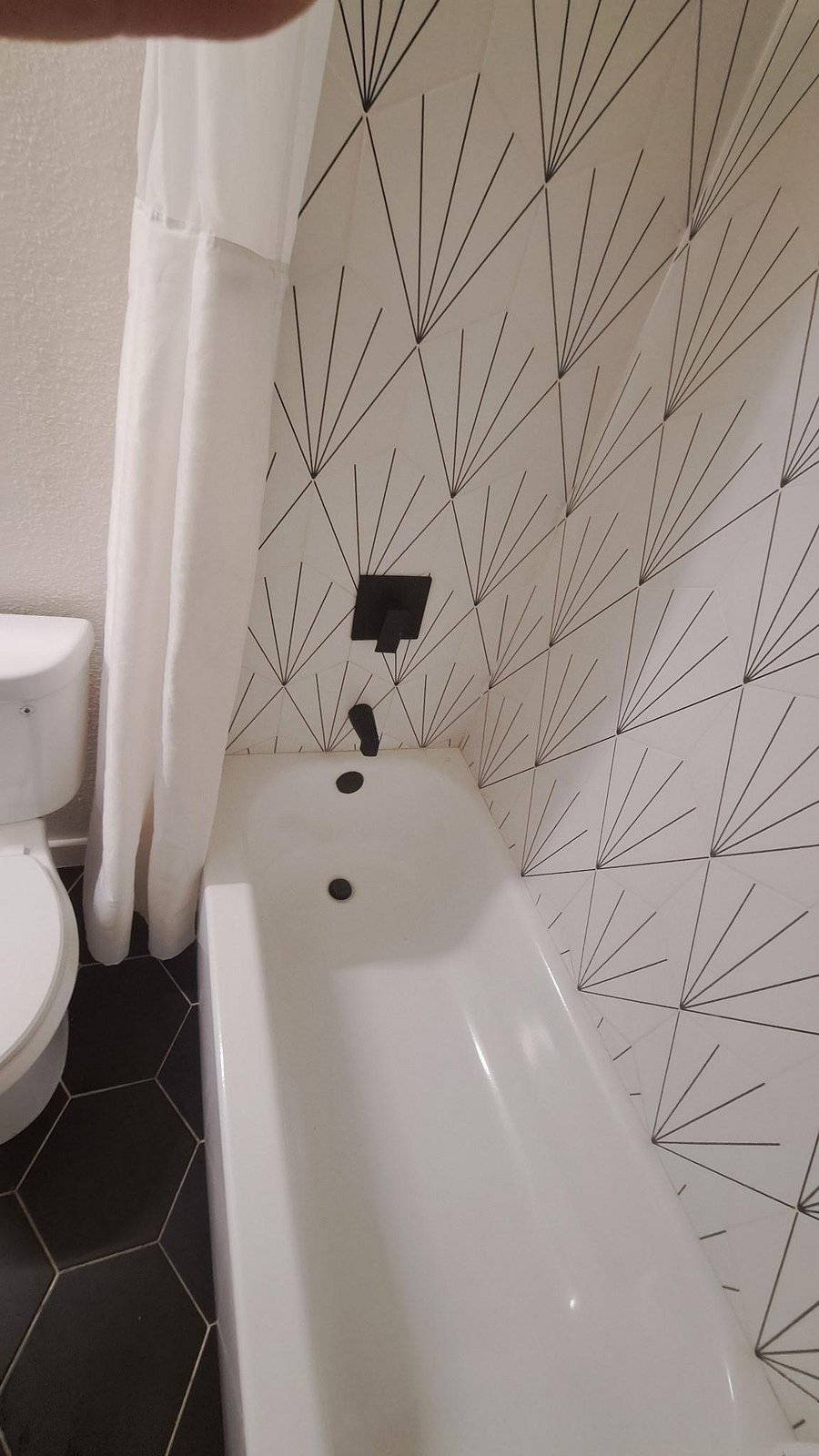Full bathroom with a tub/shower combo, patterned tile surround, and matte-black fixtures for a clean, updated look.