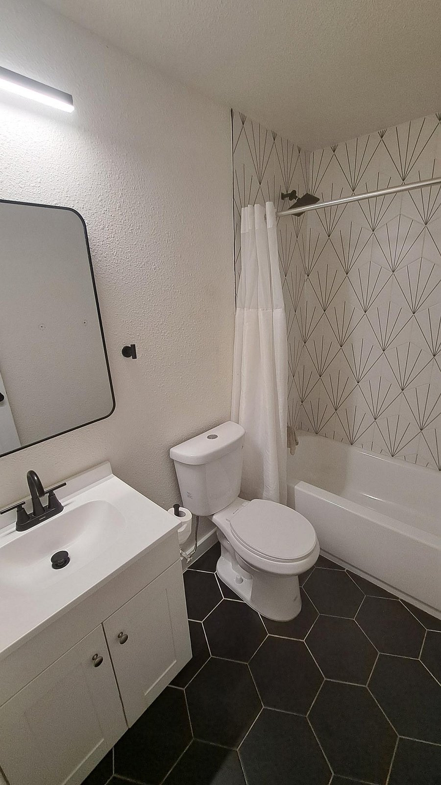 Updated full bath with tub/shower combo, patterned accent wall, and vanity with under-sink storage.
