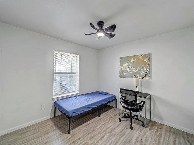 Simple bedroom with a twin bed, desk setup, ceiling fan, and a window with blinds for comfortable everyday living.