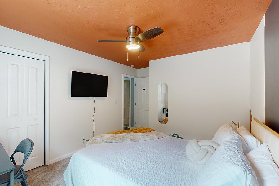 This Queen bedroom is equipped with a ceiling fan, work desk and a chair, luxurious mattress, lamps, side tables and a closet