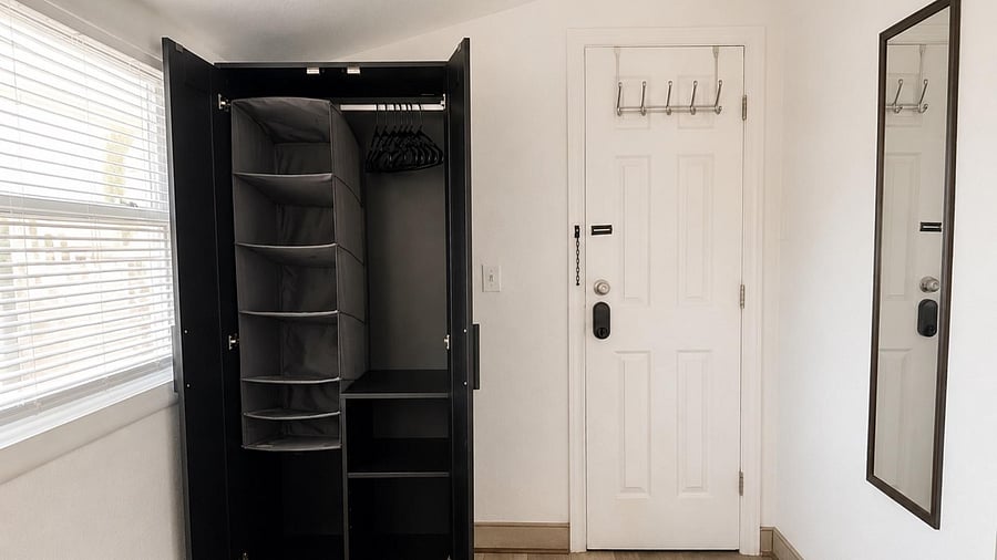 Entry area includes a freestanding wardrobe with hanging space and shelving, plus wall hooks and a full-length mirror.
