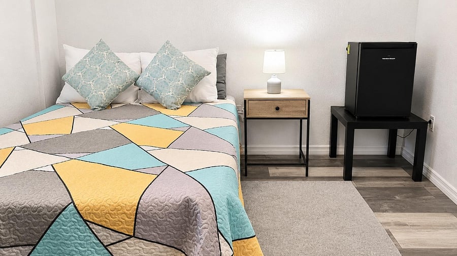 Furnished bedroom with a nightstand, lamp, and an in-room mini fridge for added convenience.