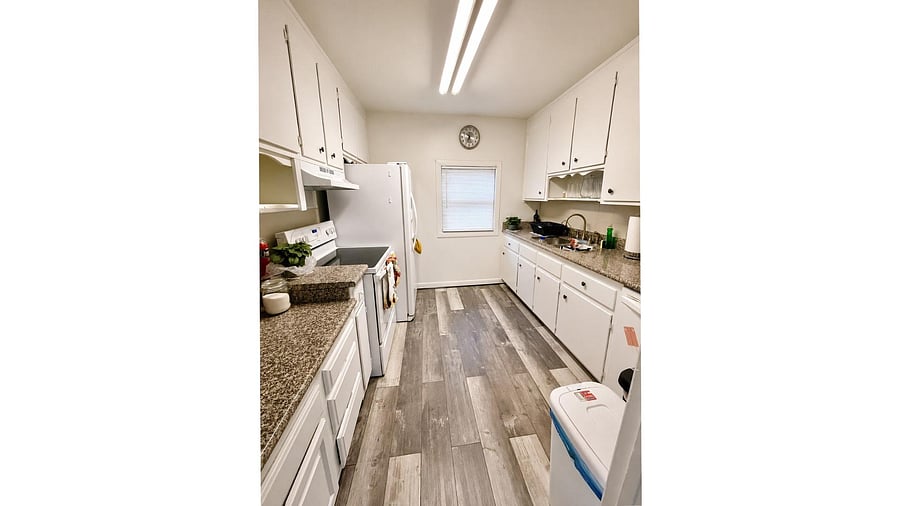 Galley-style kitchen with ample cabinet storage, stone counters, and full-size appliances plus a window.