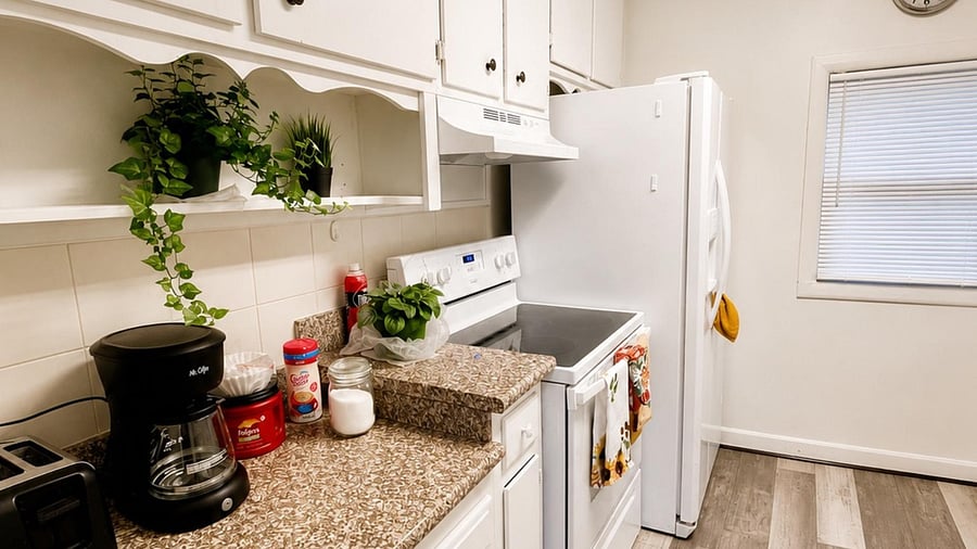 Efficient kitchen with ample cabinetry, stone counters, electric range, full-size refrigerator, and a window for ventilation.