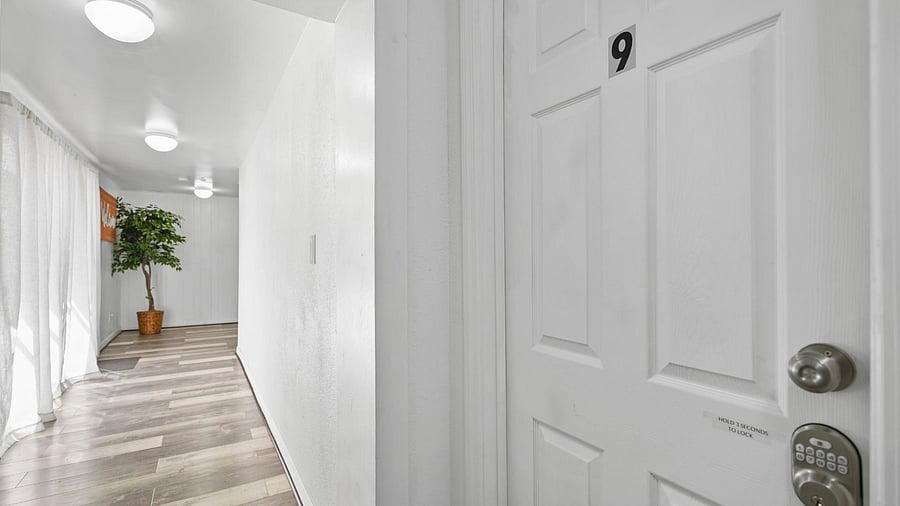 Wide hallway with durable plank-style flooring, overhead lighting, and privacy doors for individual rooms.
