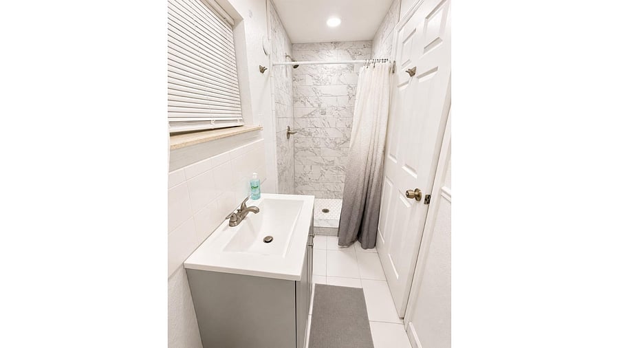 Updated bathroom with a sleek vanity, tile flooring, and a walk-in shower with marble-look surround and curtain.