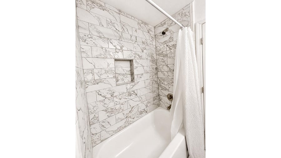 Tub/shower combo with marble-look tile surround, built-in niche shelving, and modern fixtures for easy daily use.
