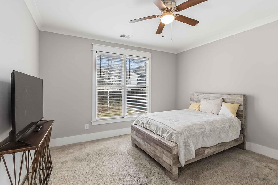 Spacious bedroom with a large window and blinds, ceiling fan, and ample room for a full bed and dresser setup.