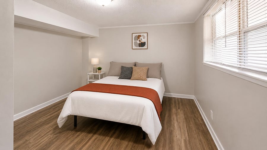 Spacious bedroom with wood-style flooring, a large window with blinds, and room for a nightstand or small desk.