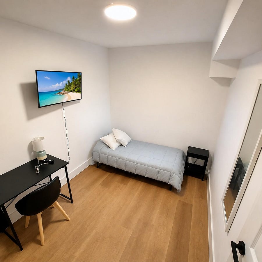 Efficient furnished bedroom with a twin bed, desk workspace, wall-mounted TV, and wood-style flooring for easy upkeep.