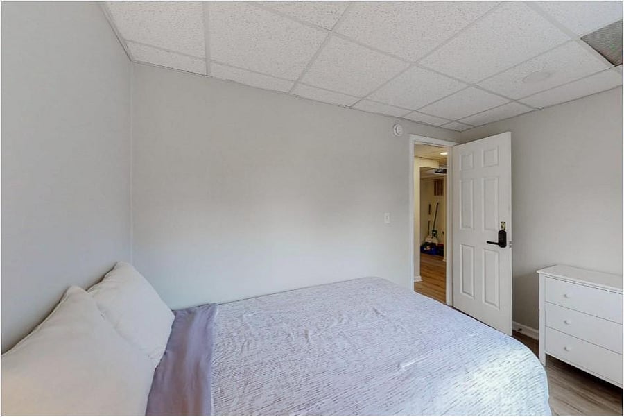 Private bedroom with a full-size bed, neutral walls, and space for a dresser, with easy access to the hall.