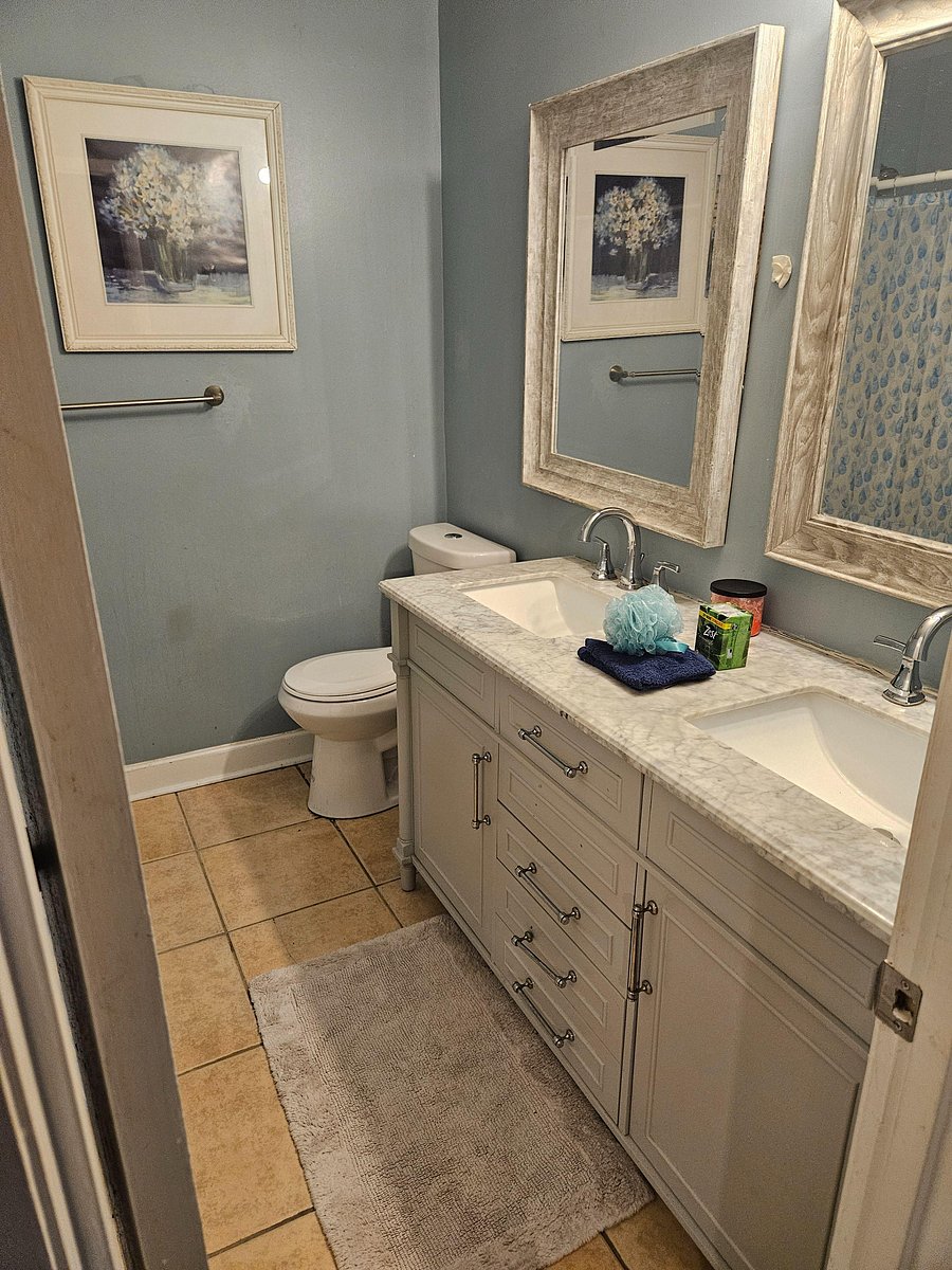 Full bathroom with double-sink vanity, ample storage, and a tub/shower combo with tile flooring.
