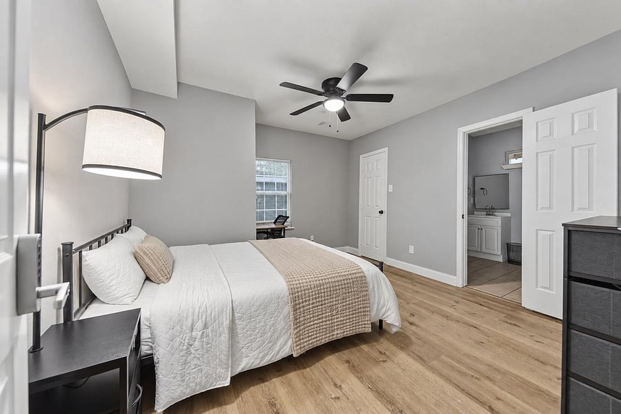 Spacious bedroom with wood-look floors, ceiling fan, and a window nook ideal for a desk, plus an ensuite vanity area.