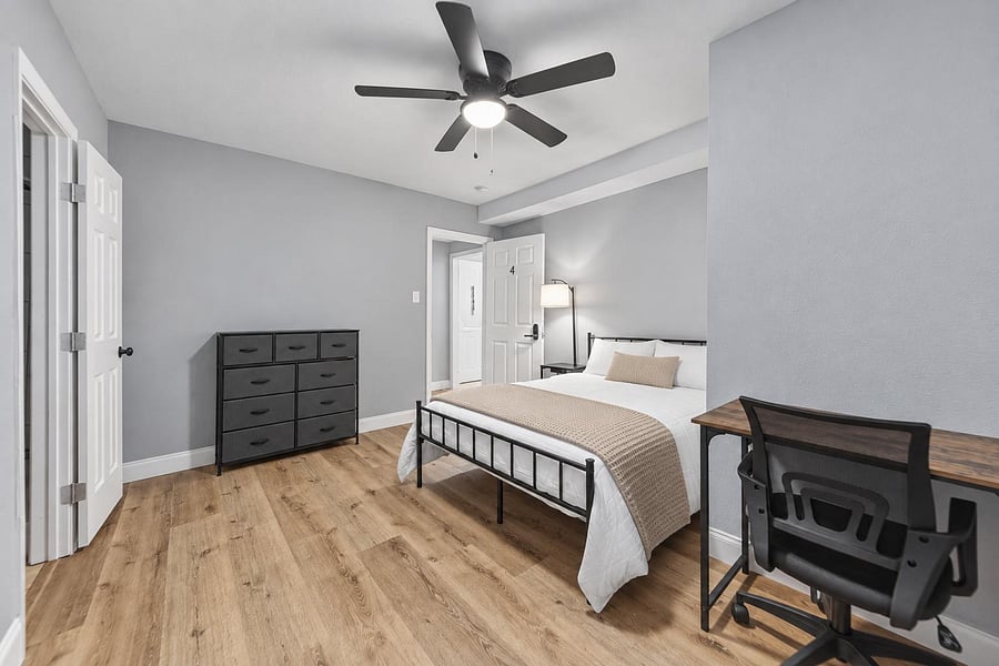 Furnished bedroom with wood-look flooring, ceiling fan light, dresser storage, and a dedicated desk for work or study.
