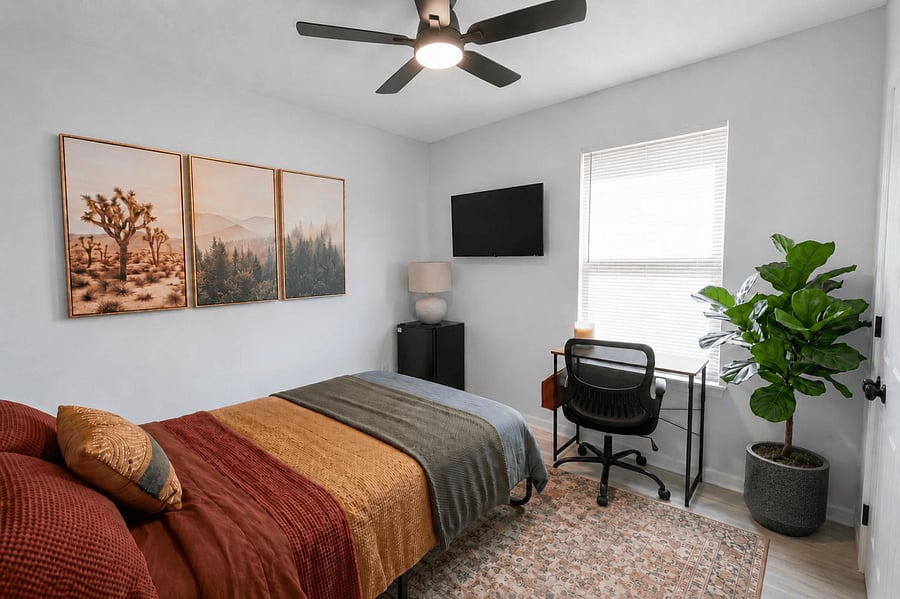 Private bedroom with ceiling fan, window blinds, wall-mounted TV, mini fridge, and a dedicated desk for working or studying.