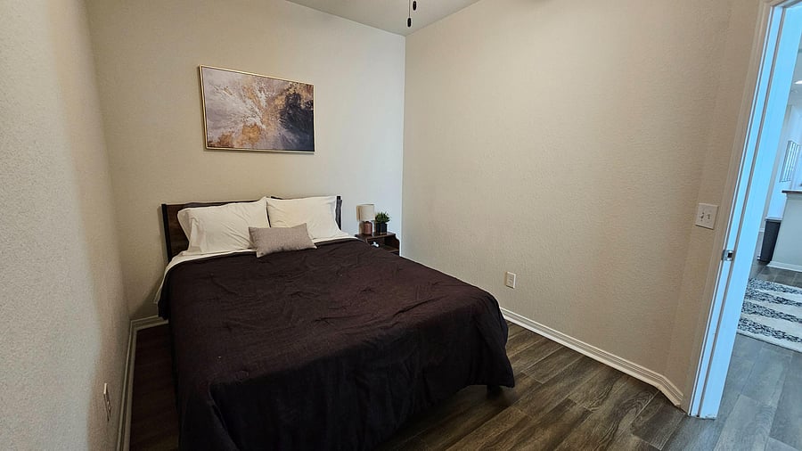 Furnished bedroom featuring a full bed, nightstand, and durable wood-look flooring with easy access to the hallway.