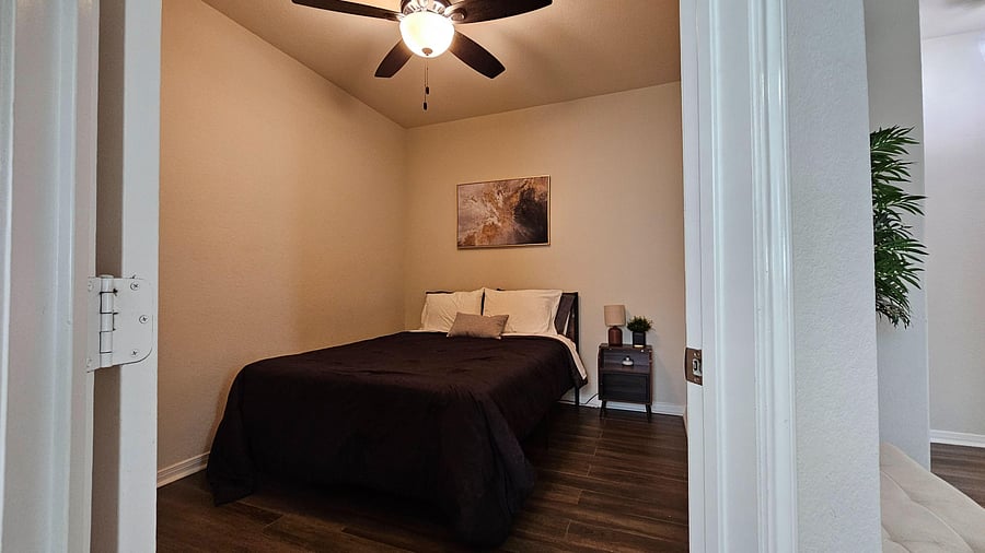 Private bedroom with a ceiling fan, queen bed, nightstand lighting, and durable wood-look flooring for easy upkeep.