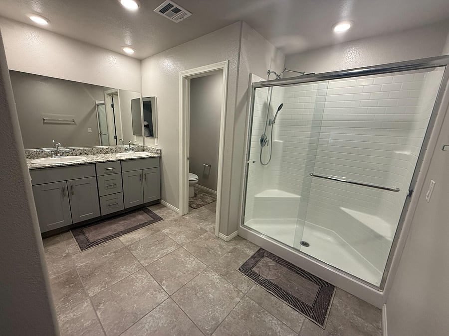 Spacious bathroom with dual-sink vanity, granite countertop, and a glass-enclosed tub/shower with handheld sprayer.
