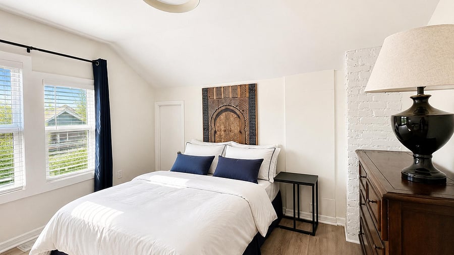 Bedroom features a full bed, side table, dresser, and large windows with blinds for natural light and privacy. Small desk