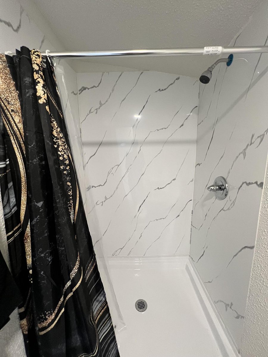 Tub/shower combo with marble-look wall panels, a fixed showerhead, and a curtain rod for easy daily use.