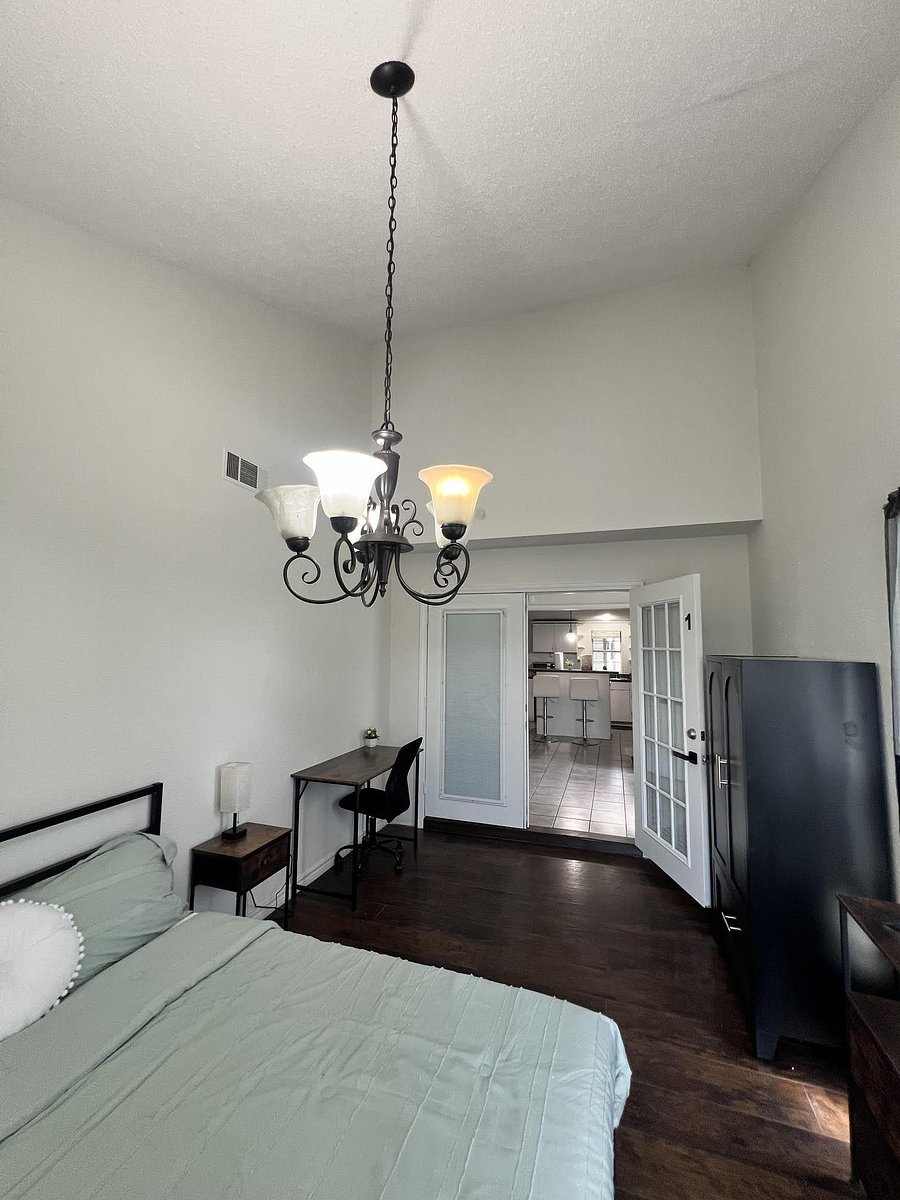 Private bedroom with high ceilings, wood floors, a study desk, dresser storage, and French-door access to common areas.