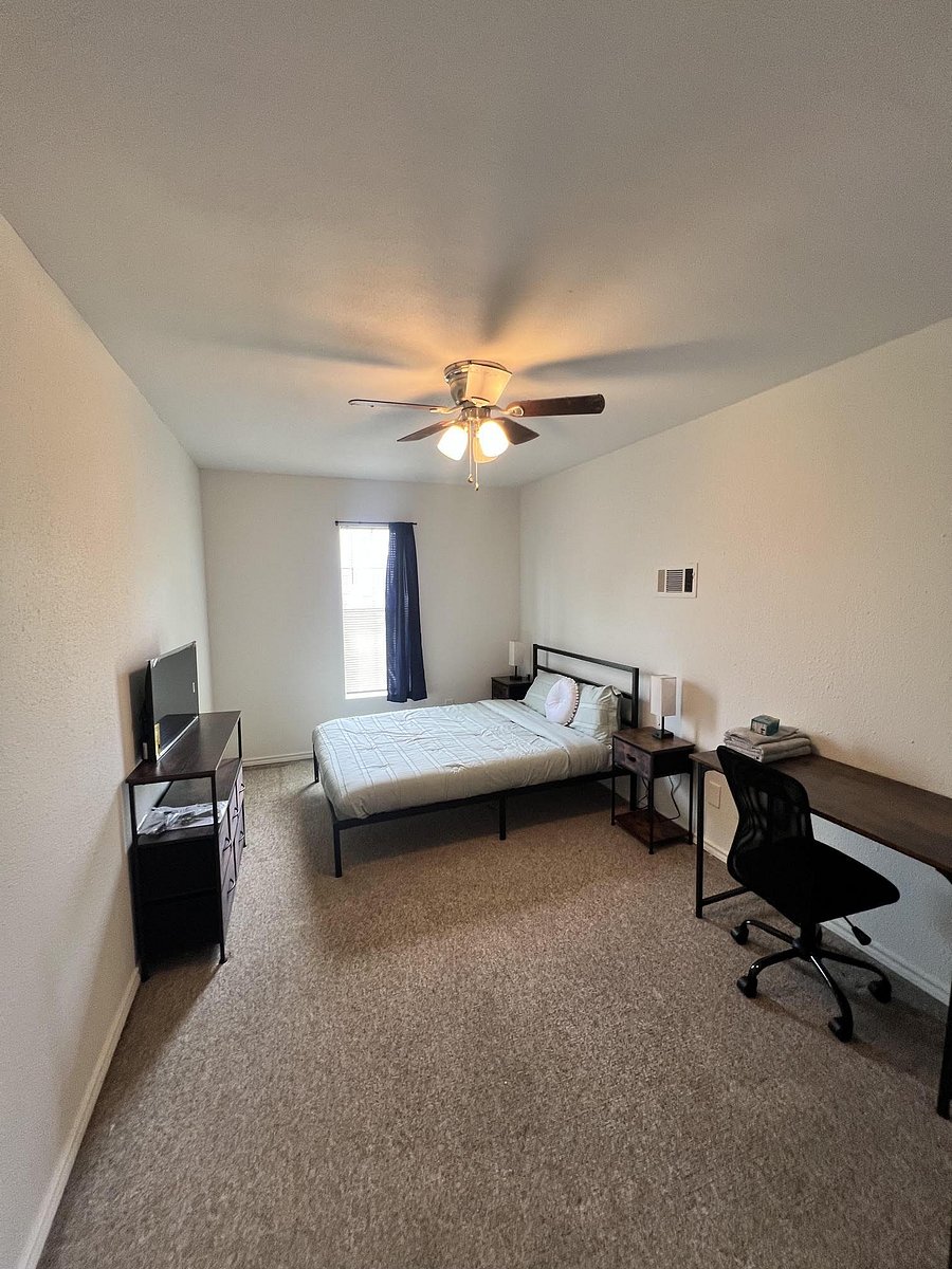 Furnished bedroom with a full bed, nightstands, desk workspace, and a TV stand, plus a window and ceiling fan.