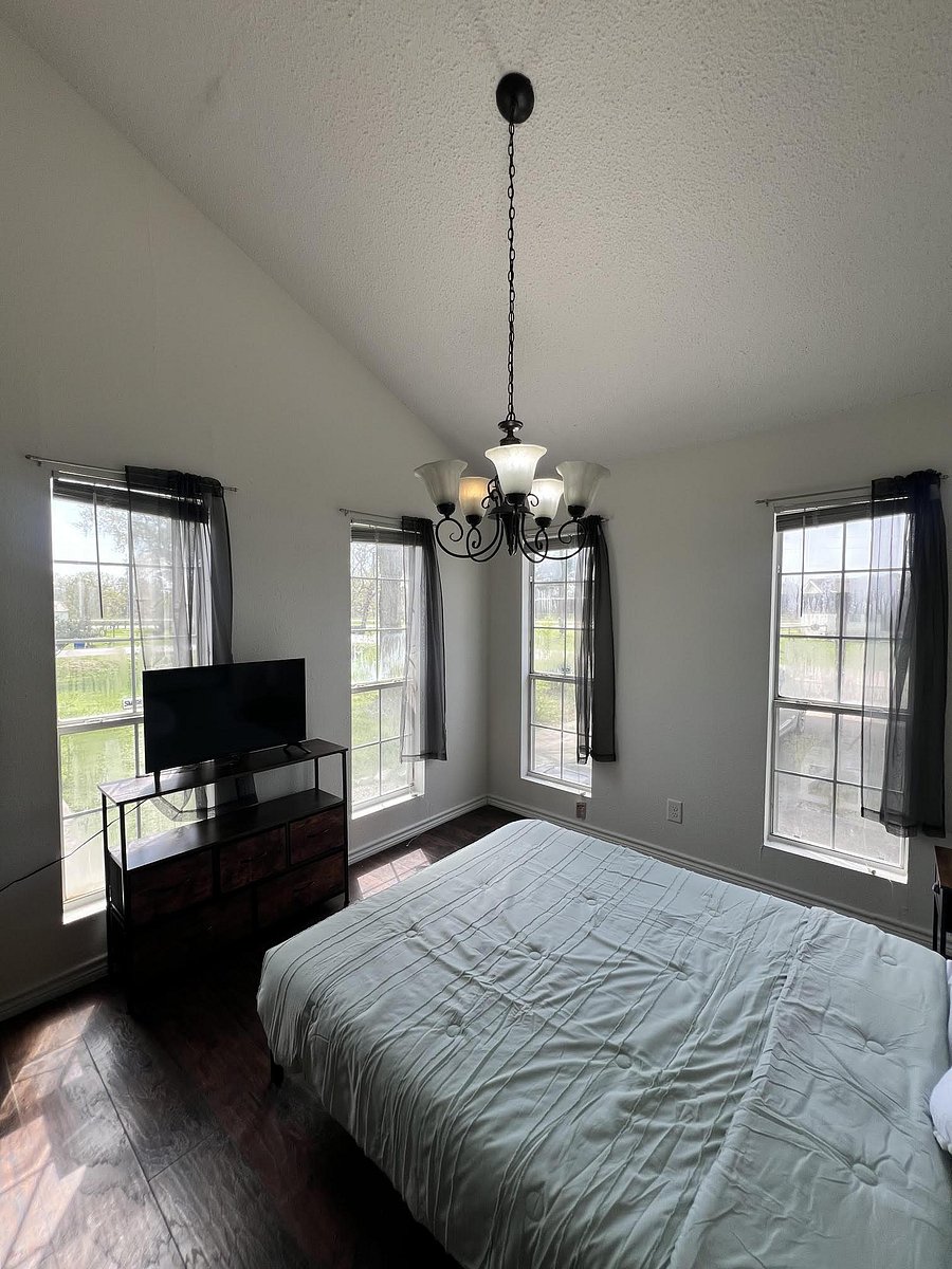Spacious bedroom with three large windows, dark wood flooring, and an overhead chandelier for comfortable everyday living.