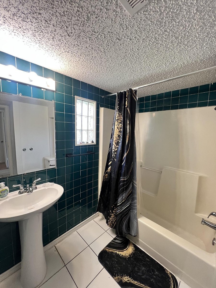 Full bathroom with shower/tub combo, tiled walls, pedestal sink, and a glass-block window for natural light.
