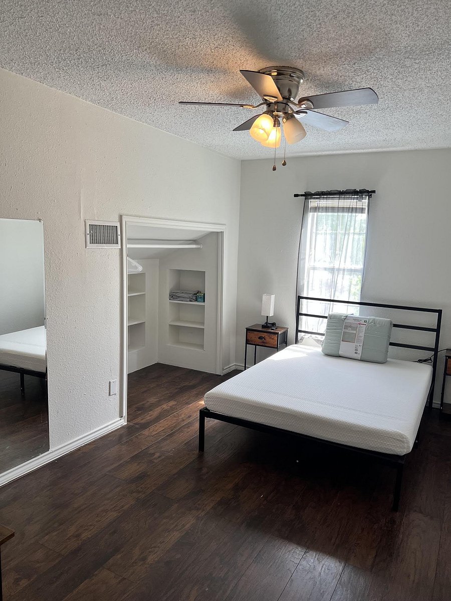 Furnished bedroom with a ceiling fan, wood-look flooring, window with curtains, and an open closet with built-in shelving.