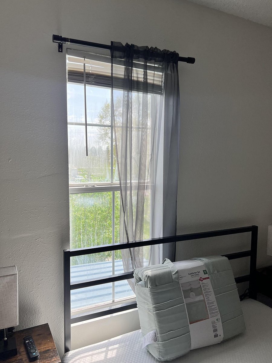Bedroom features a large window with blinds and sheer curtains, offering natural light and a relaxing outdoor view.