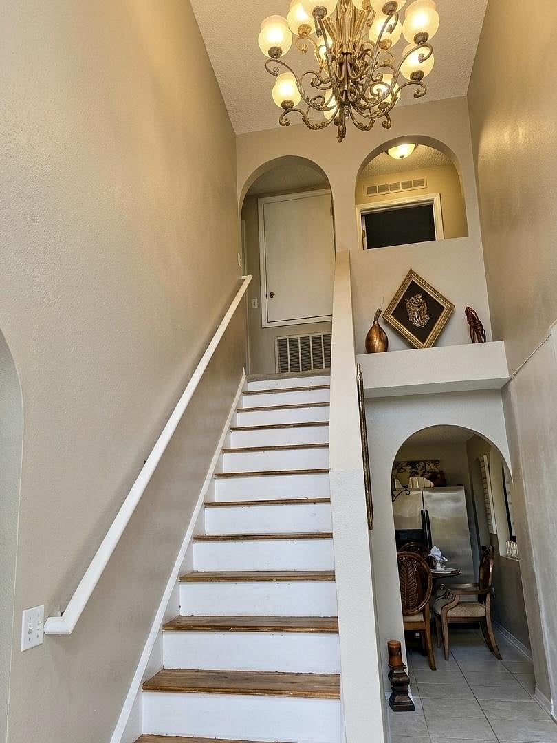 Two-story entry hall with staircase, high ceiling, and statement chandelier, opening to an adjacent dining area.