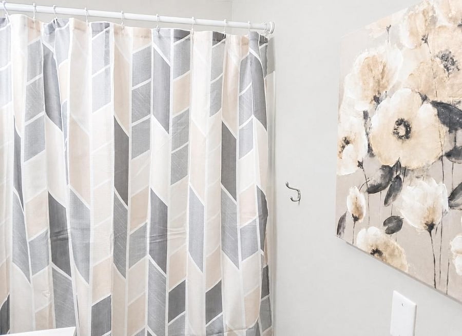 Clean bathroom tub/shower combo with patterned shower curtain, neutral walls, and decorative wall art.