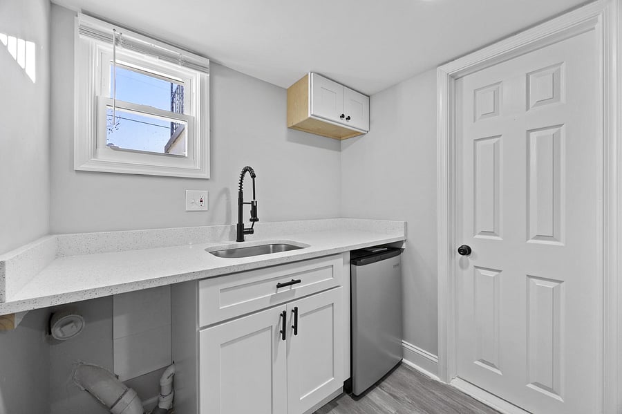 Compact kitchenette with stone-look counters, undermount sink, shaker cabinetry, and a mini fridge with window light.