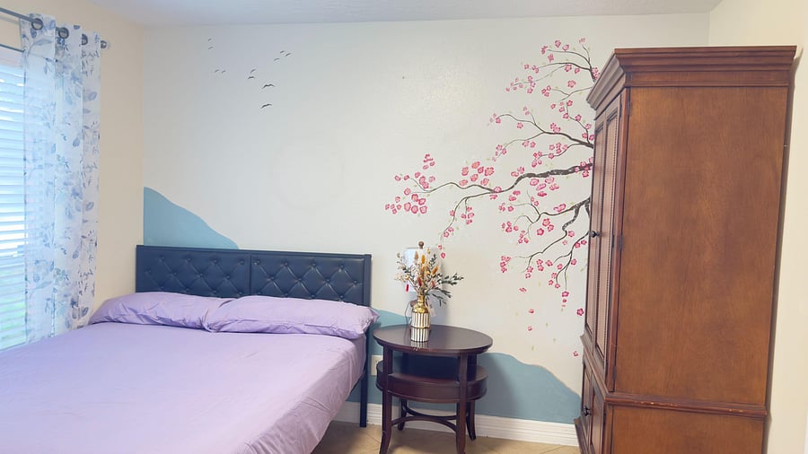Furnished bedroom with a full bed, side table, and wardrobe storage, plus a window with blinds and curtains.
