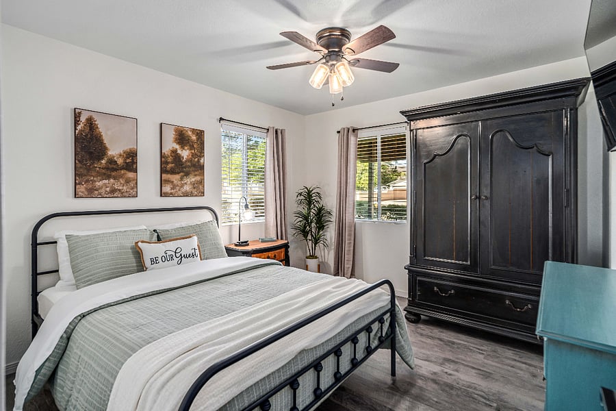 Primary Bedroom  Queen-size farmhouse-style bed, warm black-and-wood furnishings, a large armoire for ample storage, a ceiling fan, wall-mounted Smart TV, and extra linens for added comfort.