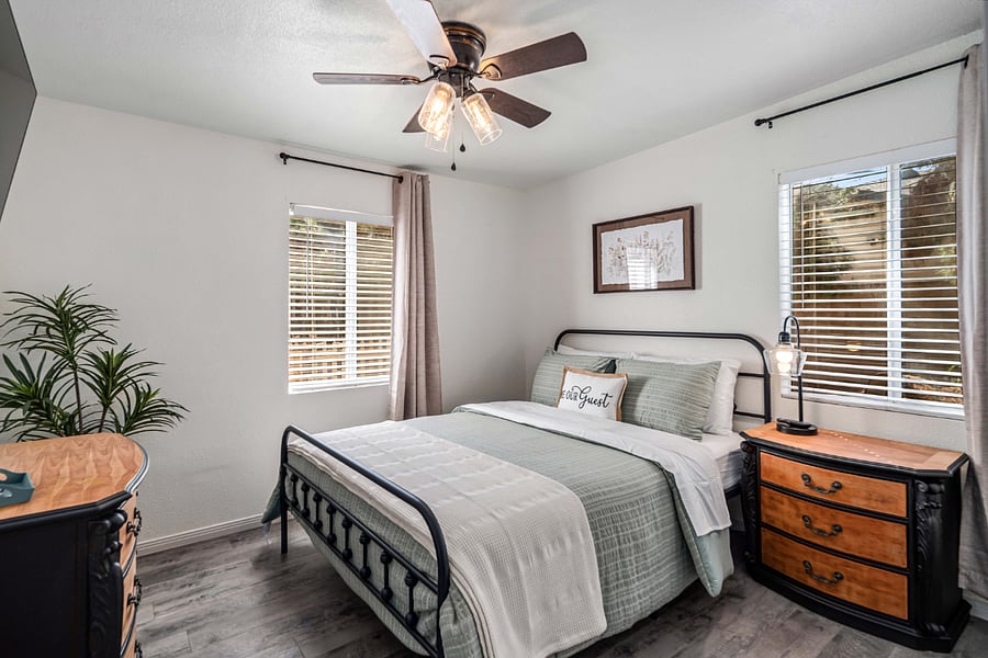 Second Bedroom  Queen-size farmhouse-style bed, clean black-and-white tones, a spacious dresser, barn door closet, large windows that provide abundant natural light, a ceiling fan, wall-mounted Smart TV, and extra linens.