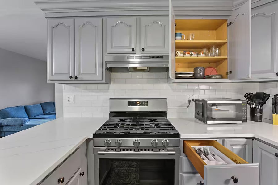 Kitchen with a stove, oven, refrigerator, freezer, dishwasher, toaster, blender, and hot water kettle, cooking basics, baking sheets, dishes, silverware, wine glasses, and a coffee maker with coffee.