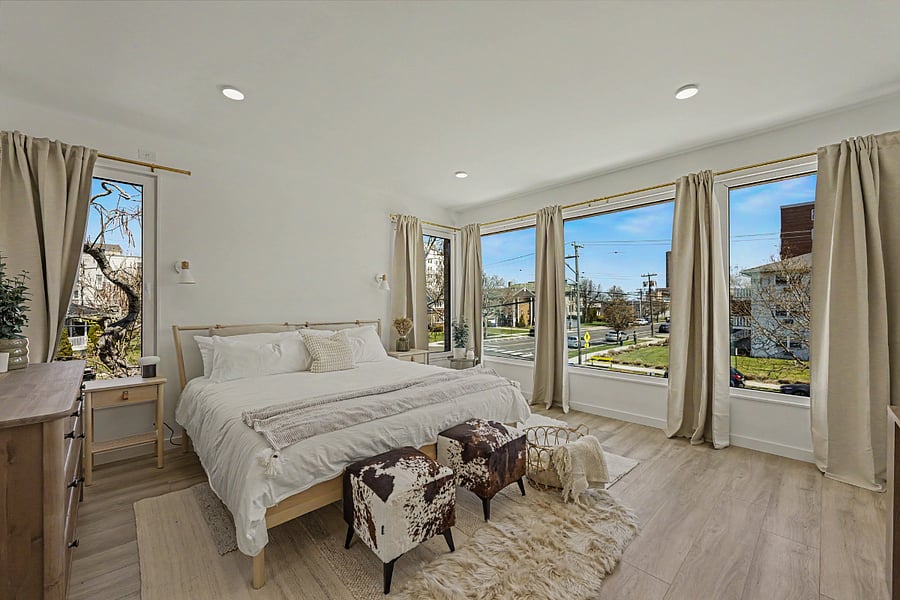 The primary from the opposite corner. Soft light, layered textures, full-length mirror by the dresser. Designed to sleep the way your own bedroom does.