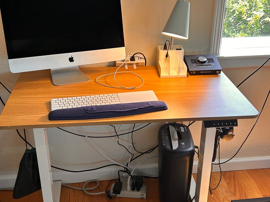 Adjustable height work desk 3 1/2 feet wide by 2 1/2 feet deep, charging station and hooks for hanging headphones and cables.