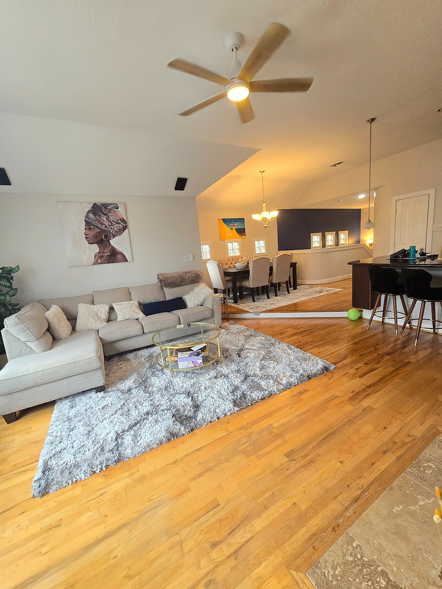 Spacious open-concept living and dining area featuring vaulted ceilings, hardwood floors, and modern furnishings. The bright, inviting space flows seamlessly from the kitchen to the living room, creating the perfect setting for relaxing or entertaining.