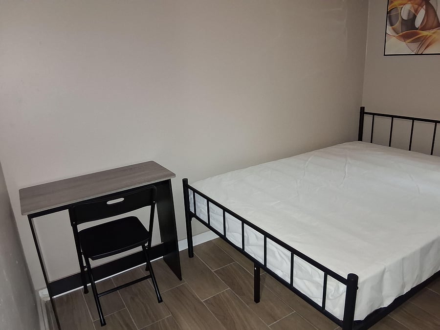 Furnished bedroom featuring a metal bed frame, Workstation with desk with chair, and durable tile flooring for easy upkeep.