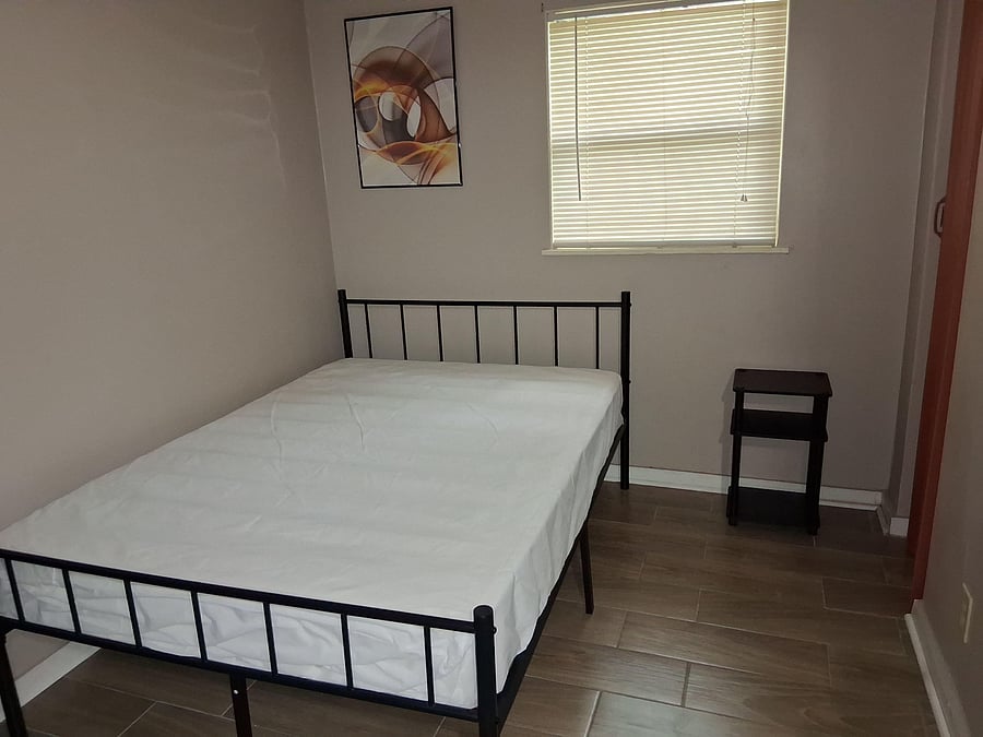 Private bedroom with a metal bed frame, tile flooring, and a window with blinds for light and privacy.