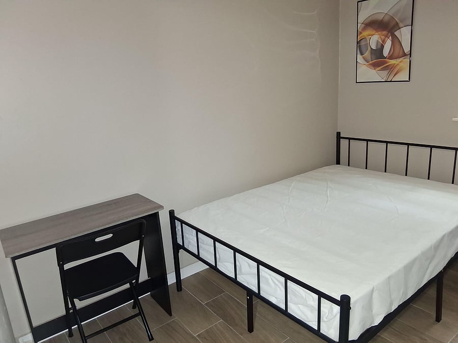 Furnished bedroom with a metal bed frame, tiled floors, and a compact desk setup for work or study.