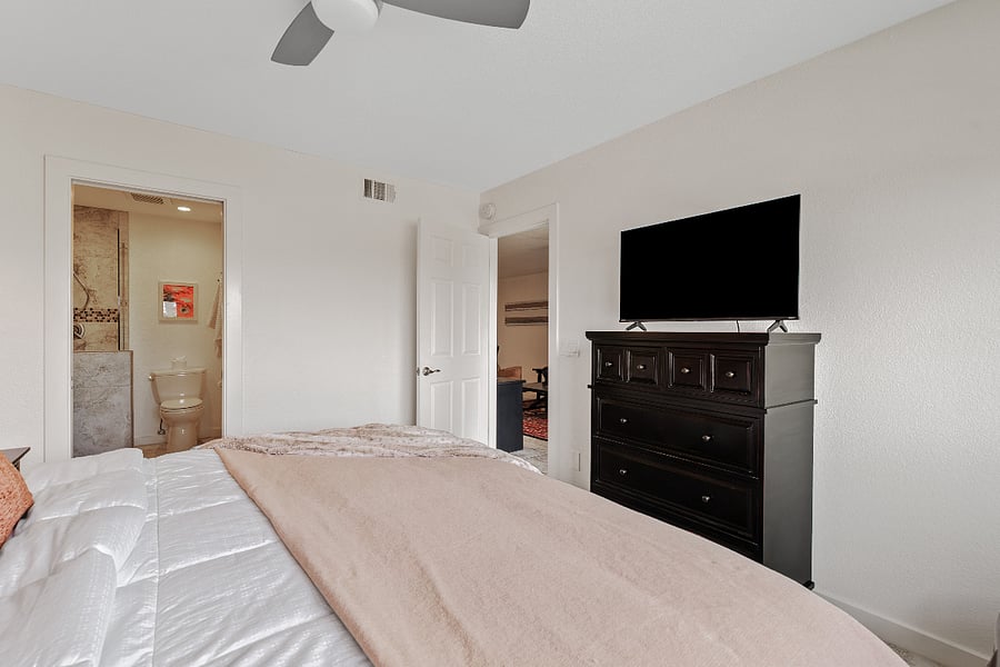 Cozy, sunlit Primary bedroom 1 with a king bed, private ensuite bathroom, TV, and peaceful views of the surrounding grounds.
