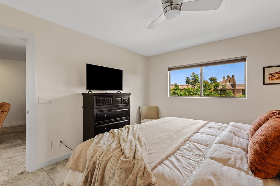 Cozy, sunlit Primary bedroom 1 with a king bed, private ensuite bathroom, TV, and peaceful views of the surrounding grounds.